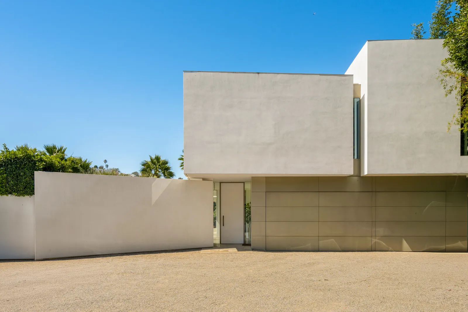 Street elevation of Stradella Residence, a white plaster residence with a walled motor court