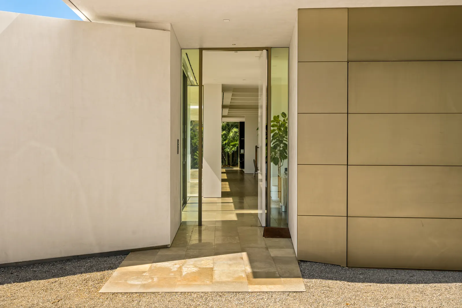 Entry at Stradella Residence, a pivoting door set into a plaster wall with a view through the house