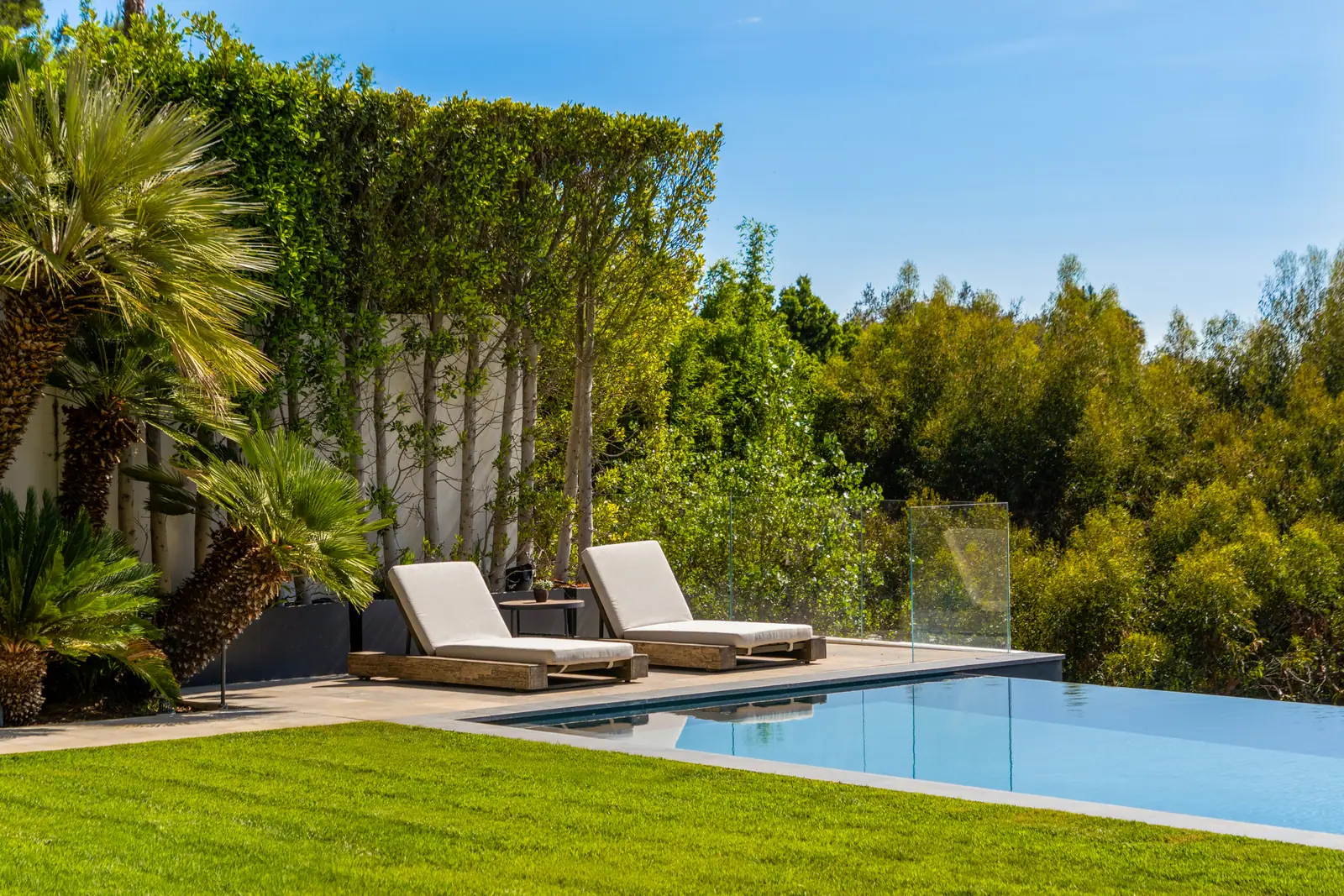 Loungers on the lawn at the pool edge with trees beyond