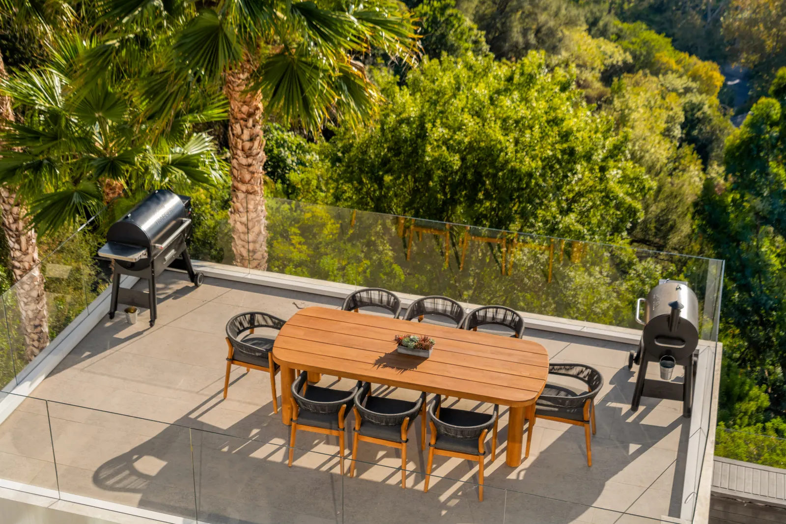Rooftop dining terrace with a long wood table and grill